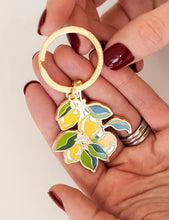 Load image into Gallery viewer, Hand holding a keychain with lemon design on a plain background