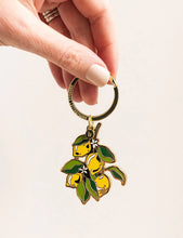 Load image into Gallery viewer, Hand holding a keychain with lemon design on a light background