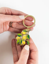 Load image into Gallery viewer, Hand holding a keychain with lemon design on a white background