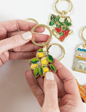Load image into Gallery viewer, Hand holding a keychain with lemon design against a white background