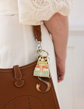 Load image into Gallery viewer, Brown handbag with a decorative keychain featuring books