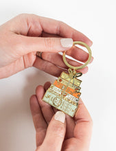 Load image into Gallery viewer, Hand holding a gold keychain with decorative design on a white background