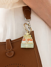 Load image into Gallery viewer, Keychain with book stack design attached to a brown leather bag.