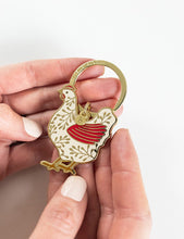 Load image into Gallery viewer, Hand holding a decorative keychain with a red and gold rooster design on a white background