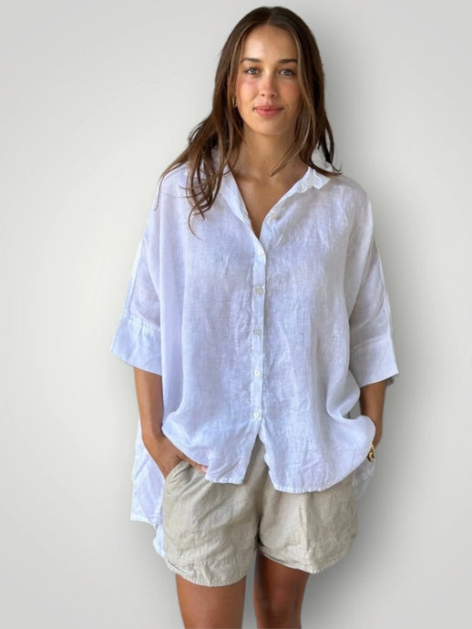 Woman wearing a white linen shirt and beige shorts against a plain background