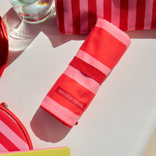 Load image into Gallery viewer, Picture of red and pink striped sand-free towel rolled up on a poolside setting.