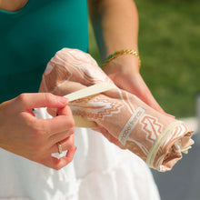 Load image into Gallery viewer, Picture of a woman undoing the elastic loop around the floral tan sand-free towel in an outside setting.